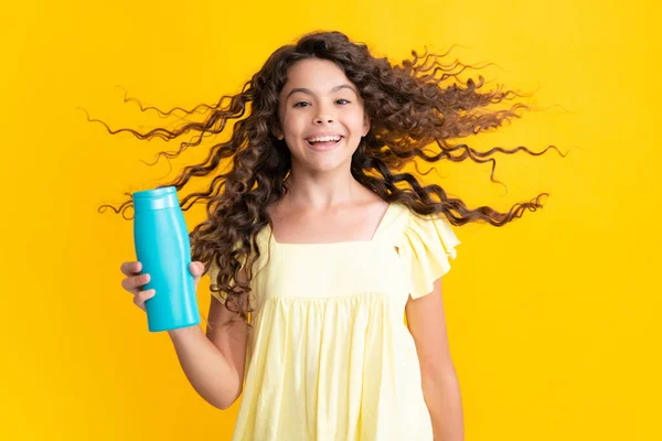 Teenager child girl showing bottle shampoo conditioners or shower gel isolated on yellow background. Hair cosmetic product. Mock up bottle. Excited teenager, glad amazed and overjoyed emotions