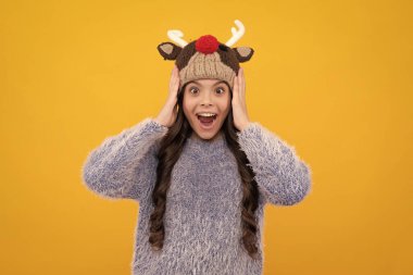 Modern teenage girl 12, 13, 14 year old wearing sweater and knitted hat on isolated yellow background. Excited face, cheerful emotions of teenager girl