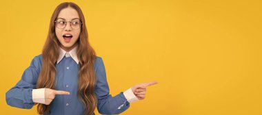 Surprised kid point fingers yellow background. Pointing for advertising. Pointing gesture, copy space. Child face, horizontal poster, teenager girl isolated portrait, banner with copy space
