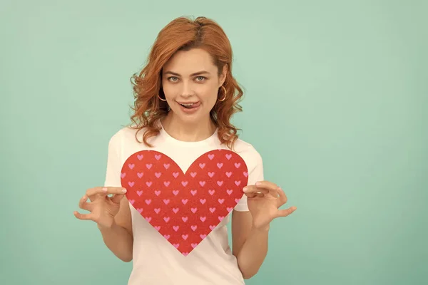 stock image smiling redhead lady hold red heart on blue background.