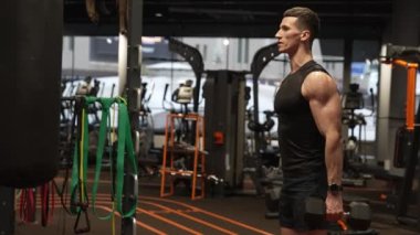 Spor salonunda dambıllarla egzersiz yapan bir sporcu. Formda olan adam spor salonunda trisepsli bukle egzersizi yapıyor. Spor ve spor. Fitness egzersizleri.