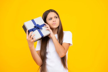 Düşünen yüz, genç kızın düşünceli duyguları. Sarı izole edilmiş arka planda hediye kutusu tutan genç bir çocuk. Çocukların doğum günü hediyesi. Noel veya Yeni Yıl hediye kutusu