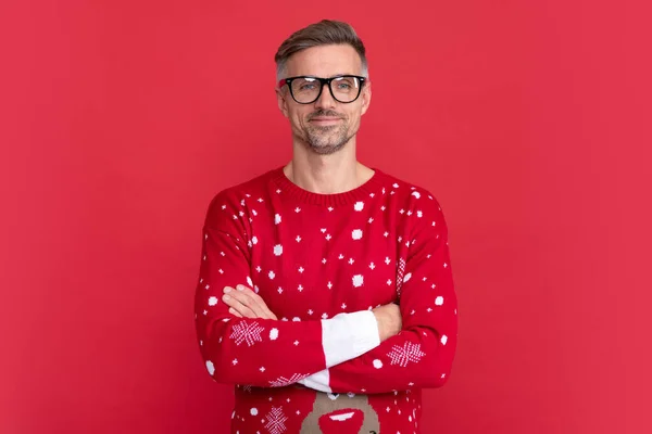 stock image smiling man in winter sweater and glasses. xmas guy crossed hands on red background. happy new year. merry christmas.