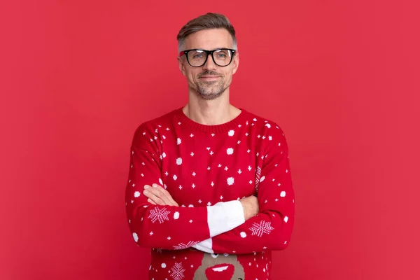 Stock image smiling man in winter sweater and glasses. xmas guy crossed hands on red background. happy new year. merry christmas.