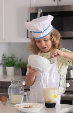 Aşçı çocuk aşçı. Yemek pişiren çocuklar. Önlüklü ve aşçı şapkalı çocuk mutfakta sağlıklı bir yemek hazırlıyor. Yemek pişirme süreci