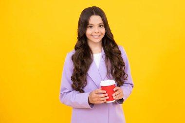 Bir fincan cappuccino kahvesi ya da çayı götüren genç kız. Sarı arka planda yemek fincanı olan çocuk, sabah içeceği. Mutlu yüz, pozitif ve gülümseyen genç kız duyguları