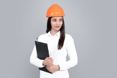 Young woman construction manager. Woman builder isolated portrait with protect helmet and clipboard. Gray background, copy space