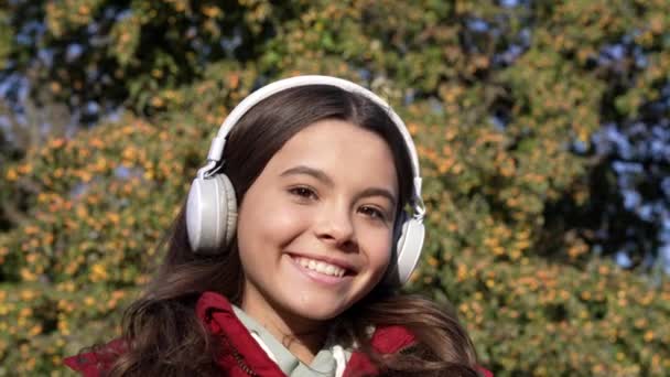ヘッドフォンの明るい10代の女の子は音楽を聞く 10代の少女の幼少期はワイヤレスヘッドフォンで音楽を聴く 10代の女の子はヘッドフォンで音楽を聴く 10代の少女のスローモーションはヘッドフォンで音楽を聴く — ストック動画