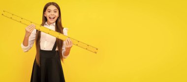 Okul üniformalı hayret bir çocuk matematik kurallarını ölçmek için elinde tutuyor. Öğrenci portresi, stüdyo afişi. Okul çocuğu yüzü, boşluklar