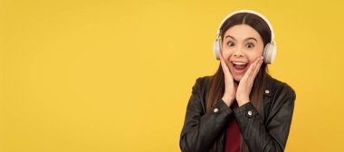 amazed child in headphones on yellow background. Child portrait with headphones, horizontal poster. Girl listening to music, banner with copy space