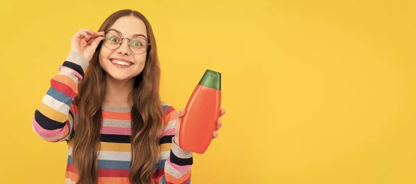 シャンプーボトルをプレゼントするメガネの明るい子供の長い髪 子供の女の子のヘアケアのバナー コピースペース付きスタジオポスターヘッダー — ストック写真