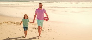 Baba ve oğul plajda futbol ya da futbol oynuyor. Mutlu baba ve oğul yaz plajında top ve aileyle yürür..