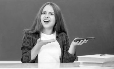 Okulda kafası karışık bir çocuk telefonda karatahta arka planında sohbet ediyor, SMS.