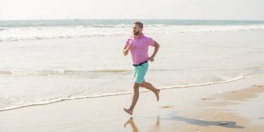 Enerjik bir yaz. Koşucu özgürlüğü hisseder. Sabahın tadını çıkarıyorum. Spor atleti okyanusta kazanmak için hızlı koşar. Sabah sporu aktivitesi. Sahilde koşan sağlıklı bir adam..