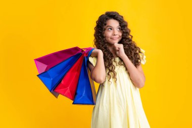 Sarı arka planda alışveriş torbaları olan güzel moda kızı. Alışveriş ve moda alışverişi. Alışveriş çantalı çocuk. Düşünen yüz, genç kızın düşünceli duyguları.