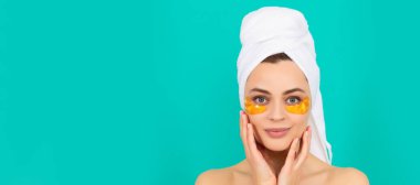 Göz bantları, göz altı bantları. Gülümseyen genç kızın yüzünde havluyla kolajen altın göz bantları var. Güzel kadın, izole edilmiş yüz portresi, taklit alanı olan pankart.