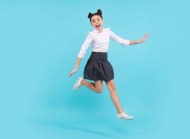 Mutlu komik zıplayan gençler. Mutlu liseli kız, pozitif ve gülümseyen genç kız duyguları. Mavi stüdyodaki genç kızın uzun atlayışı günlük etek ve gömlek giyer.