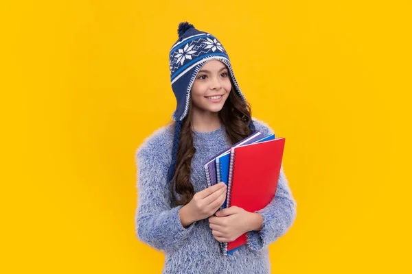 School children in winter hat and sweater with school books on isolated yellow studio background. Children learning and education