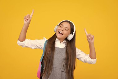 Amazed child singing. School girl, teenager student in headphones on yellow isolated studio background. Music school concept