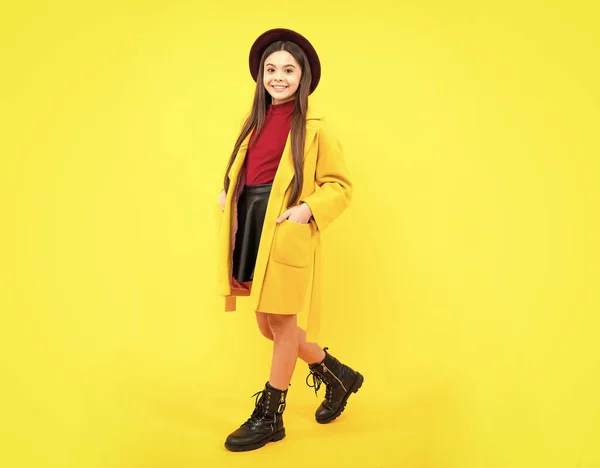 Full length of cheerful teenager child girl wearing comfy trendy fashion autumn coat, isolated over yellow background. Happy teenager portrait. Mock up copy space