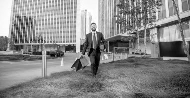 Alışveriş poşetleri ve hediye kutusuyla ofisin dışında erkek erkeğe yürüyen başarılı bir adam..