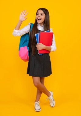 Okul çocuğu, okul çantalı genç kız izole edilmiş sarı stüdyo geçmişi üzerine kitap tutuyor. Çocuk okulu ve eğitim konsepti