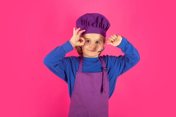 Funny kid chef cook with spoon. Chef child preparing healthy food. Studio portrait of child with chef hats