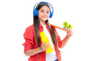 Teenagers lifestyle, casual youth culture. Teen girl with skateboard water bottle and headphones over isolated studio background. Cool modern teenager in stylish clothes
