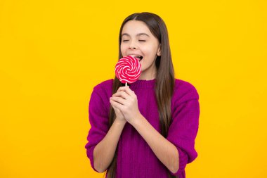 Funny child with lollipop over yellow isolated background. Sweet childhood life. Teen girl with yummy caramel lollipop, candy shop. Teenager with sweet sucker