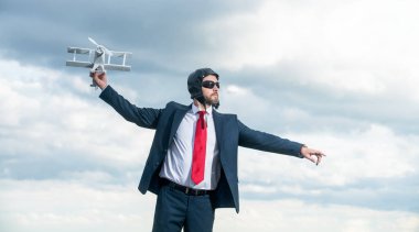 Takım elbiseli ve havacılık şapkalı iş adamı arka planda uçak fırlatma oyuncağı.