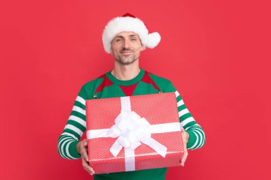 Neşeli Xmas adamı kırmızı arka planda hediye kutusunu paylaşıyor. Mutlu yıllar. Mutlu noel hediyeleri. Elf kostümlü ve Noel Baba şapkalı bir adam..