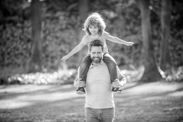 Ill give a piggy-back ride. Happy man carry son sitting on shoulders. Happy kid ride piggy-back on father. Family fun summer outdoors. Childhood and parenthood.