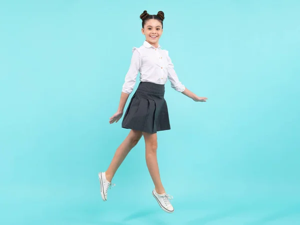 Full length jump of teenager girl on blue isolated studio wear casual skirt and shirt. Funny school girl, amazed kid genius, excited young student. Happy teenager
