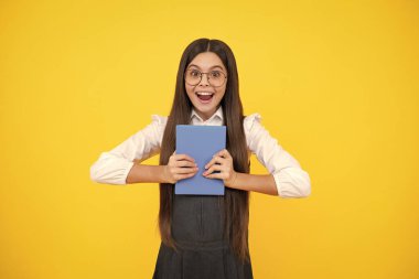 Back to school. Teenager schoolgirl with book ready to learn. School girl children on isolated yellow studio background. Excited face, cheerful emotions of teenager girl