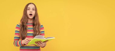 Surprised open-eyed kid hold school book yellow background, surprise. Portrait of schoolgirl student, studio banner header. School child face, copyspace