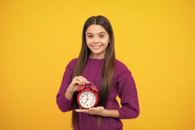 Çocuk saati sarı stüdyo arka planında izole edilmiş. Alarm saati olan genç çocuk saati gösteriyor