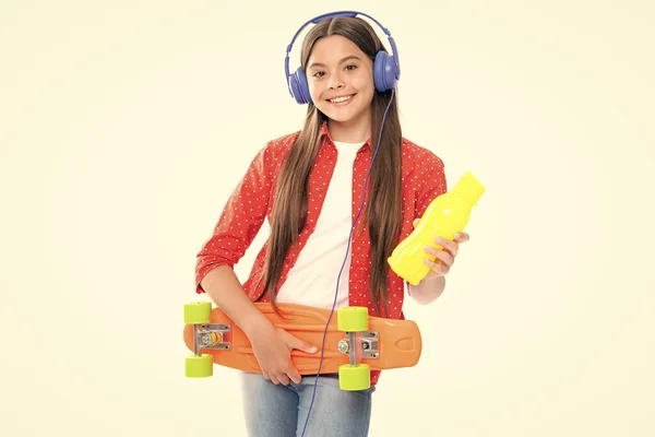 Teenagers youth casual culture. Teen girl with skateboard water bottle and headphones over isolated white background. Teenager in fashion stylish clothes. Portrait of happy smiling teenage