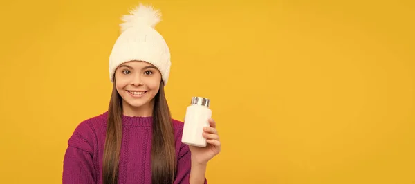 stock image smiling child in winter hat with pill jar. food supplement. teen girl with natural pill products. Horizontal poster of isolated child face, banner header, copy space