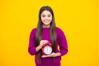 Portrait of teenage girl with clock alrm, time and deadline. Studio shot isolated on yellow background