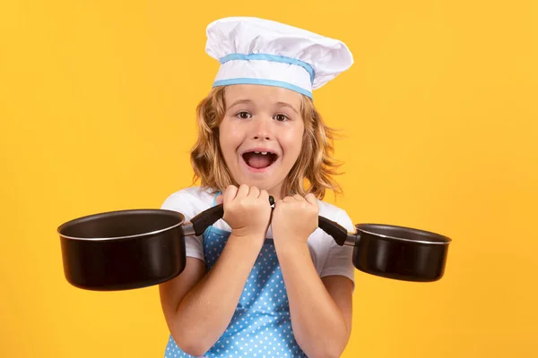 Kid chef cook with cooking pot stockpot. Child chef cook prepares food on isolated studio background. Kids cooking. Teen boy with apron and chef hat preparing a healthy meal