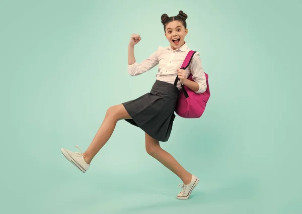 Amazed teenager. School girl in school uniform with backpack. Teenage girl student on blue isolated background. Learning knowledge and kids education concept. Jump and run. Excited teen girl