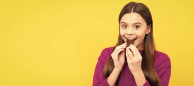 Happy girl child bite tasty chocolate slab yellow background, sweet-tooth. Horizontal poster of isolated child face, banner header, copy space