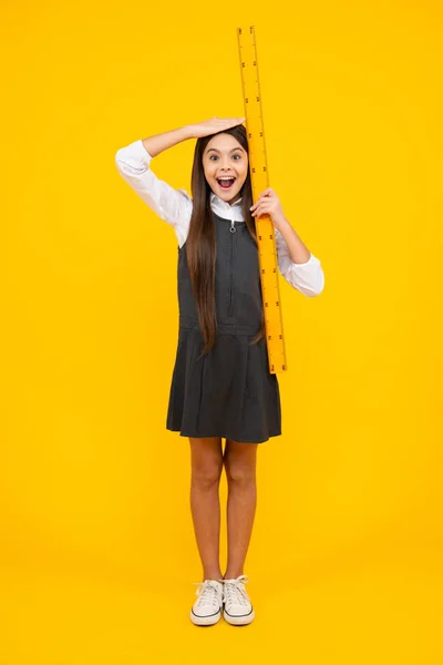 Kid height measure, growth measurement. Schoolgirl holding measure for geometry lesson, isolated on yellow background. Student study math. Excited face, cheerful emotions of teenager girl