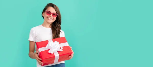 fashionable happy child in sunglasses hold gift box, shopping. Teenager girl with birthday gift, horizontal poster. Banner header with copy space