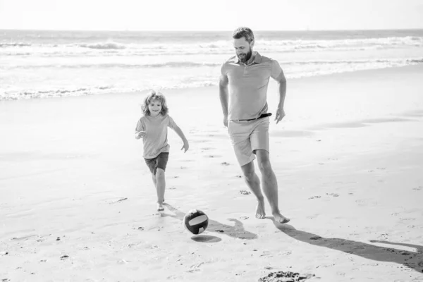 father and son playing football on summer beach, family.