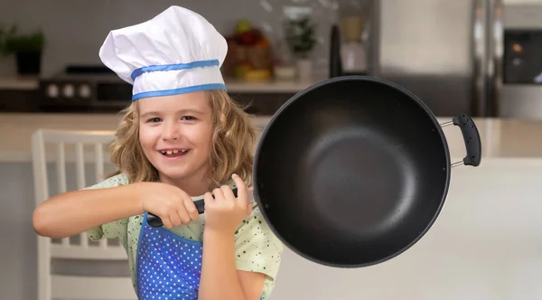 Kid chef cook cookery with pan in kitchen. Child chef cook. Funny child stand at kitchen table have fun baking, doing bakery preparing food at home kithen. Healthy food