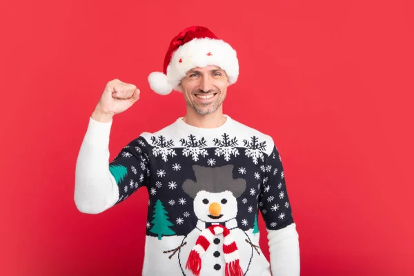 Portrait of middle aged man in sweater isolated over red background. Concept of holidays, happiness, emotions and Christmas celebration