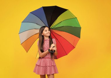 Yazlık elbise. Sarı arka planda izole edilmiş, beyaz üzerinde izole edilmiş gökkuşağı göbeği tutan mutlu genç kız. Neşeli genç çocuk güneş şemsiyesi tut