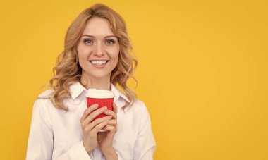 Sarı arka planda sabah kahvesi fincanı olan gülümseyen sarışın kadın..