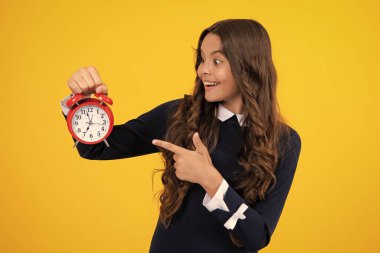 Child teenager girl with alrm clock isolated on yellow background. Time and deadline concept